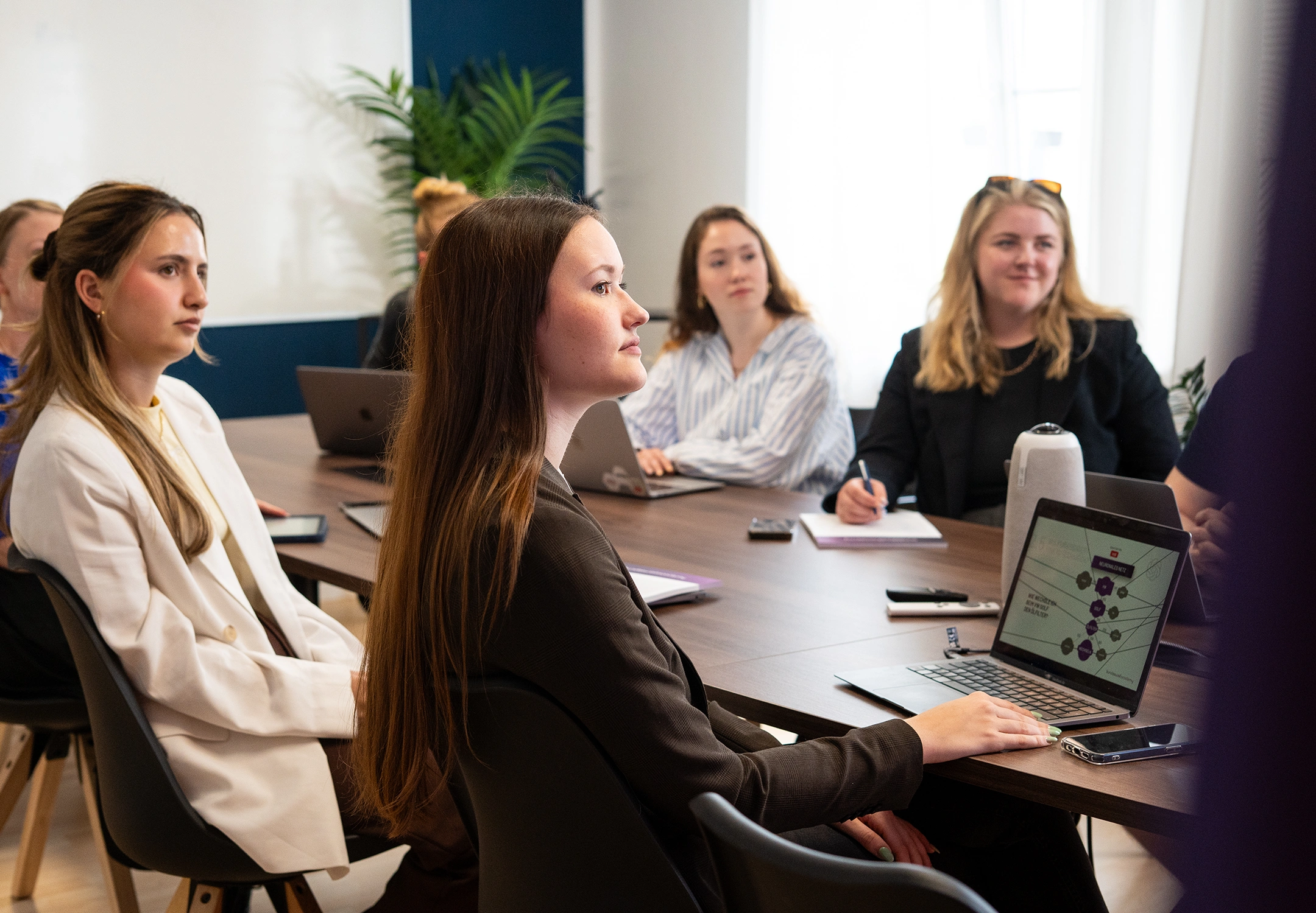 Mehrere Mitarbeiterinnen sitzen an einem Konferenztisch und schauen in eine Richtung.